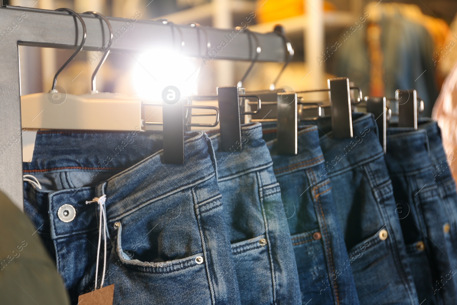 Photo of Modern jeans hanging on clothing rack in shop, closeup