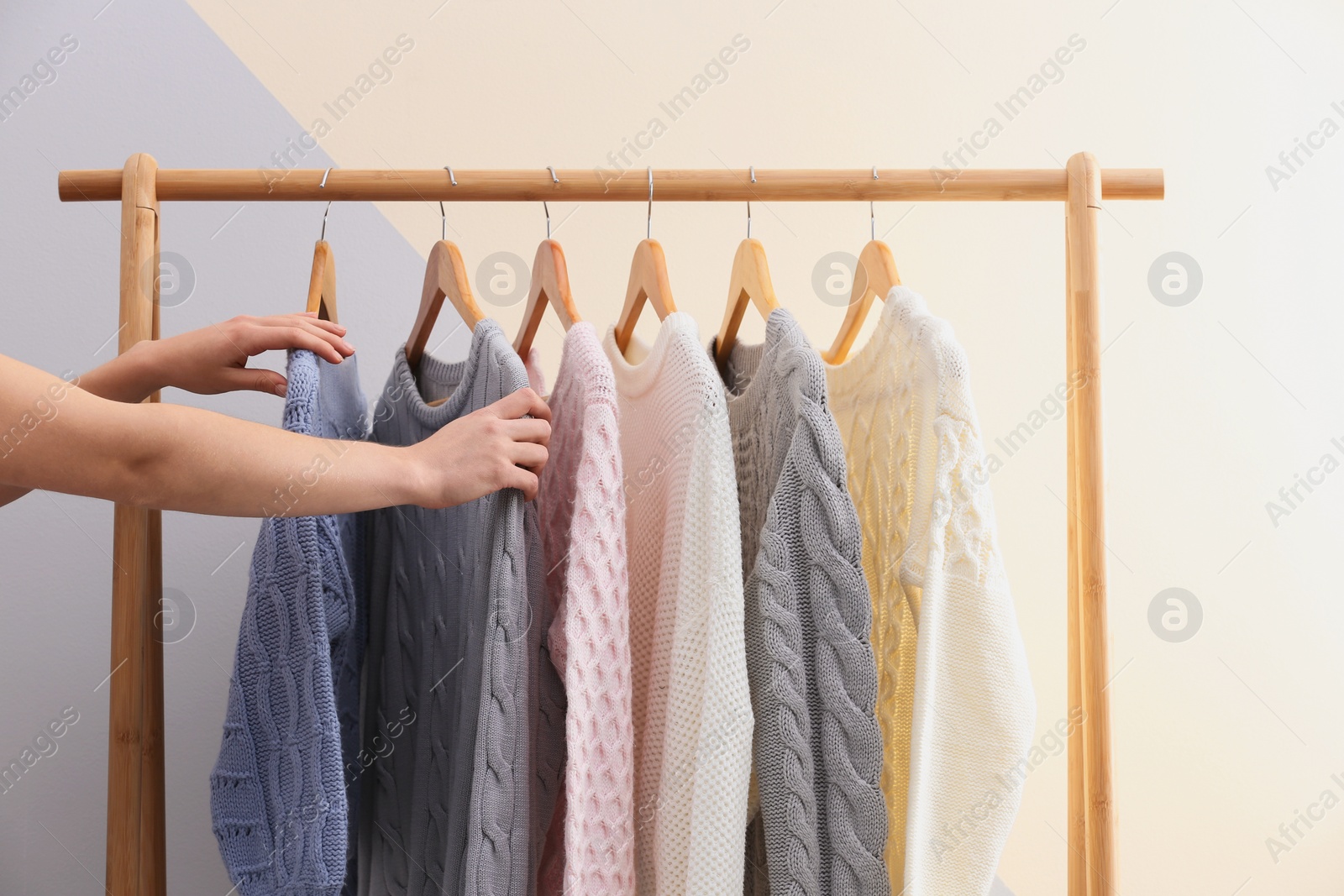 Photo of Woman choosing sweater on rack near color wall, closeup