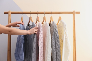 Woman choosing sweater on rack near color wall, closeup