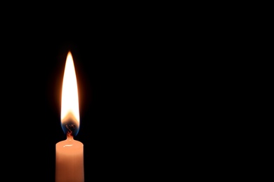 Photo of Wax candle burning on black background