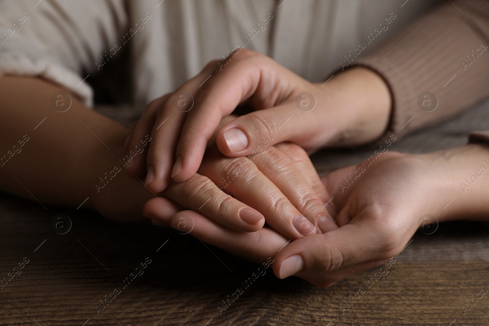 Photo of Woman holding hands with her mother at wooden table, closeup