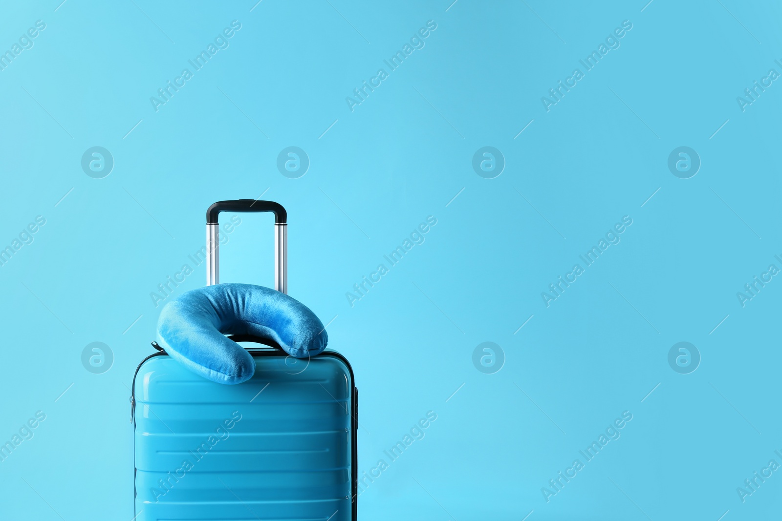 Photo of Suitcase and travel pillow on light blue background, space for text