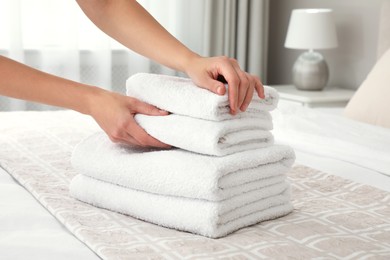 Photo of Woman putting fresh towels on bed in room, closeup