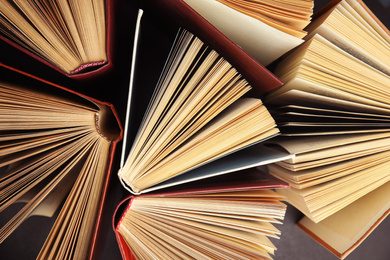 Photo of Many different hardcover books on dark background, top view