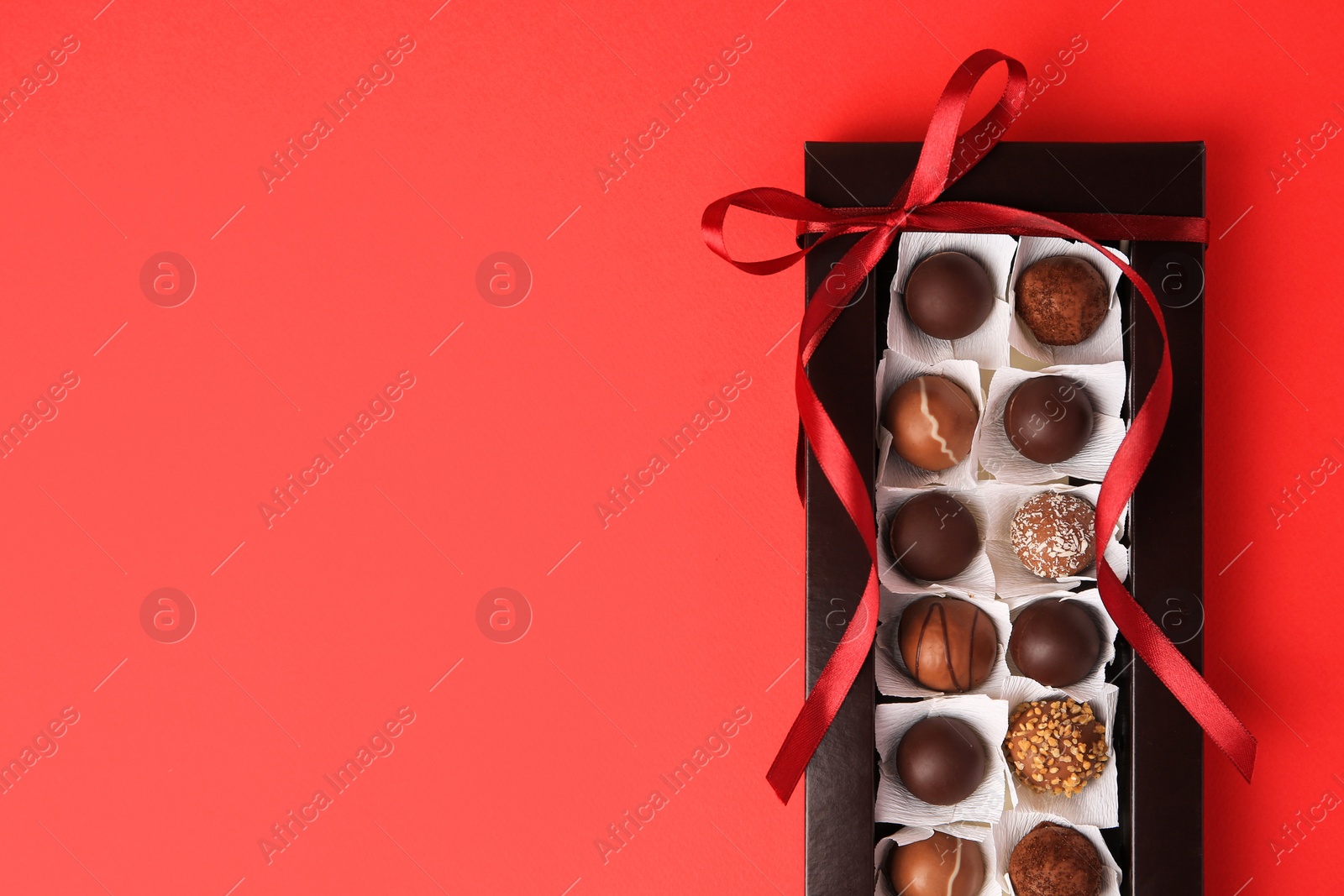 Photo of Box with delicious chocolate candies on red table, top view. Space for text