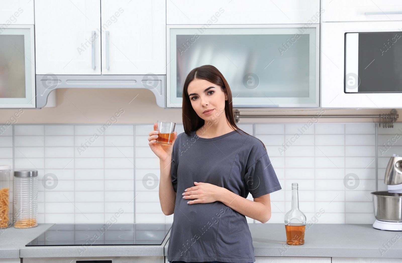 Photo of Future mother with glass of alcohol drink in kitchen. Bad habits during pregnancy