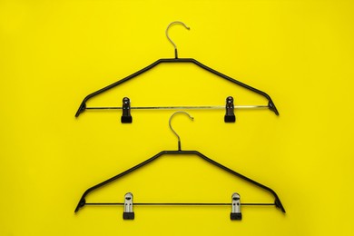 Empty hangers with clips on yellow background, flat lay