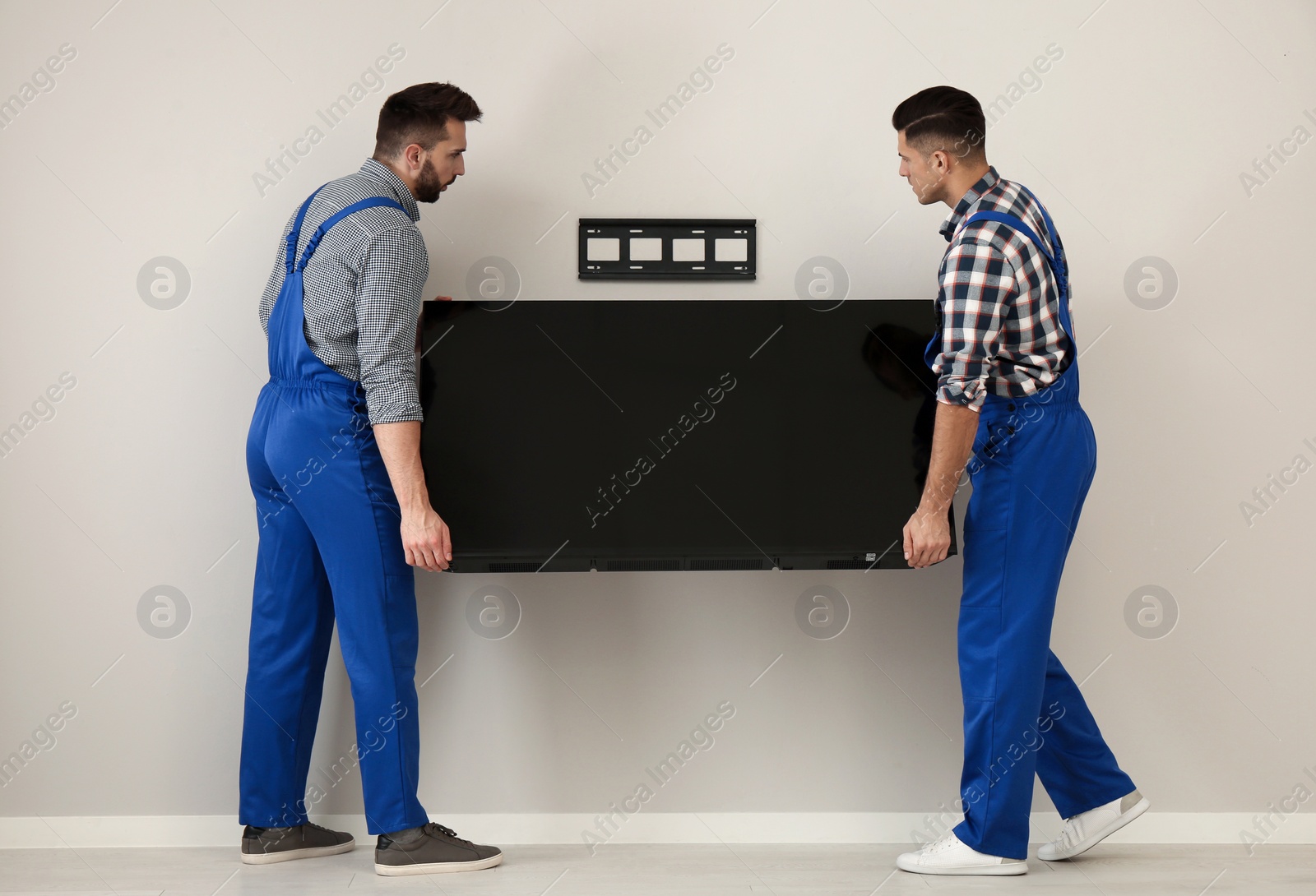 Photo of Professional technicians installing modern flat screen TV on wall indoors