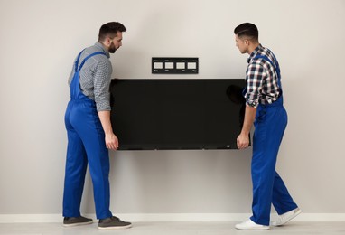 Photo of Professional technicians installing modern flat screen TV on wall indoors