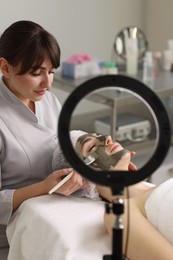 Photo of Cosmetologist applying mask on woman's face in clinic