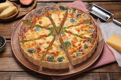 Photo of Pieces of delicious homemade quiche and ingredients on wooden table