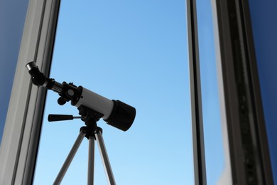 Photo of Tripod with modern telescope near open window indoors, low angle view. Space for text