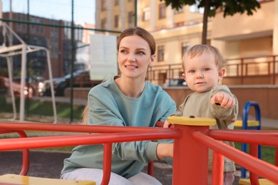 Photo of Happy nanny and cute little boy on carousel outdoors