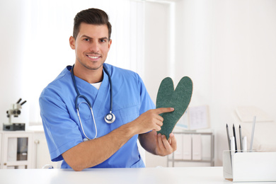 Photo of Handsome male orthopedist showing insoles in clinic