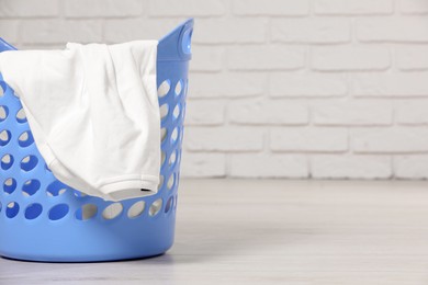 Photo of Laundry basket with clothes near white brick wall. Space for text