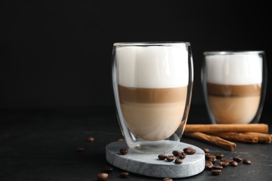 Photo of Delicious latte macchiato, cinnamon sticks and coffee beans on black table, space for text