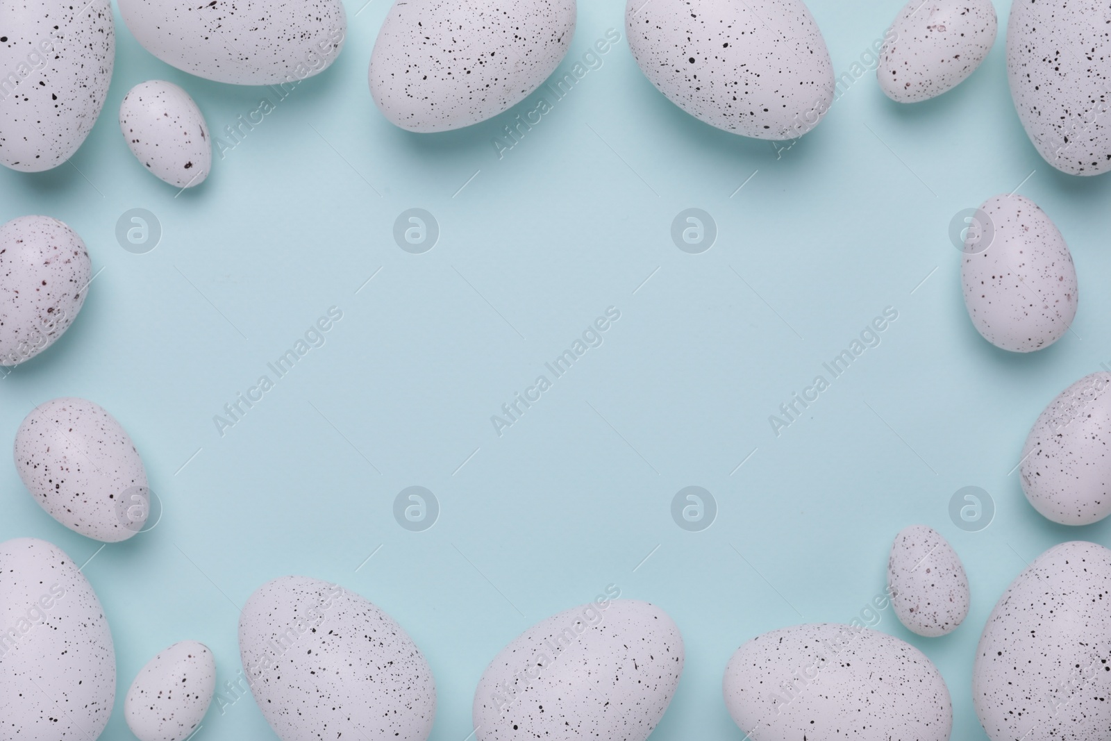 Photo of Frame of many painted Easter eggs on light blue background, flat lay. Space for text