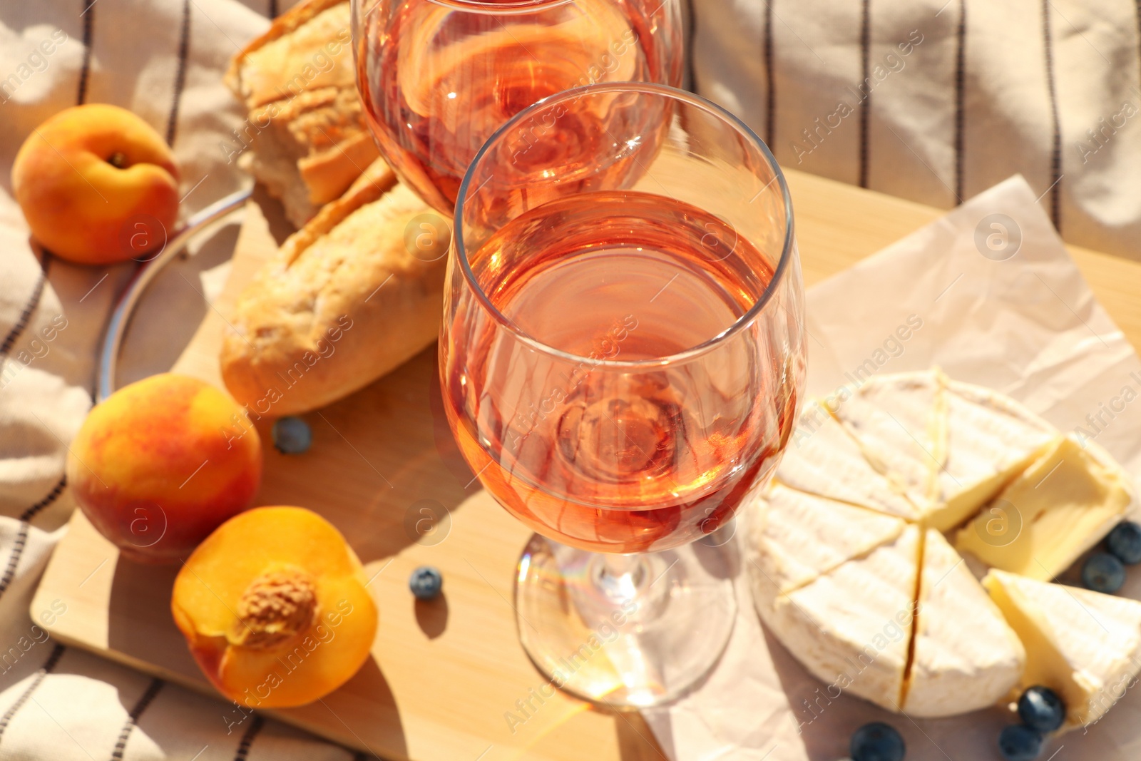 Photo of Glasses of delicious rose wine and food on white picnic blanket