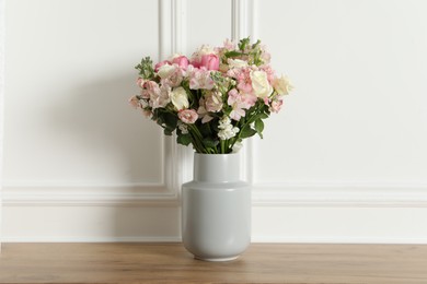 Photo of Beautiful bouquet of fresh flowers in vase on wooden table near white wall
