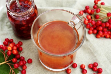 Cup of tea, jam and ripe viburnum berries on table, closeup