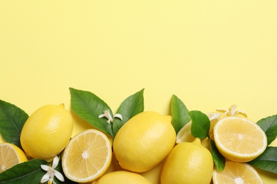 Photo of Many fresh ripe lemons with green leaves and flowers on yellow background, flat lay. Space for text