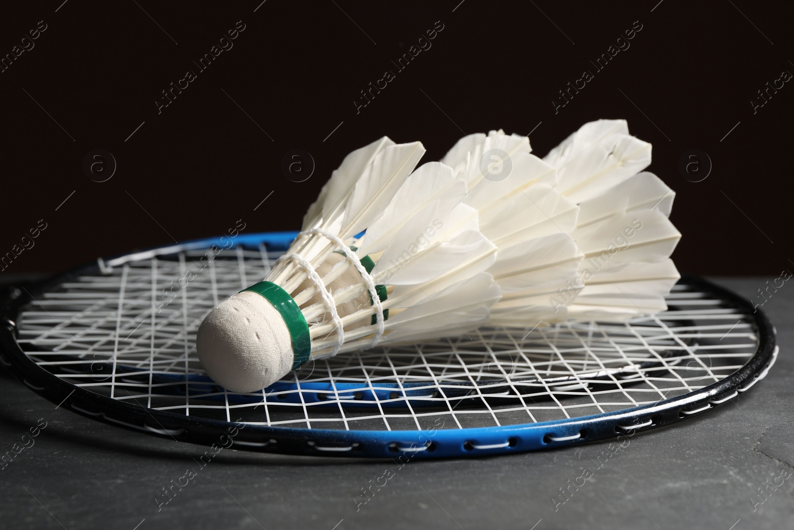 Photo of Feather badminton shuttlecocks and racket on grey table against black background, closeup