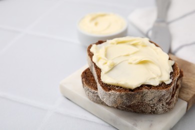 Photo of Slices of tasty bread with butter on white tiled table, closeup. Space for text
