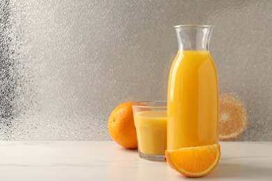 Photo of Tasty fresh oranges and juice on white marble table, space for text