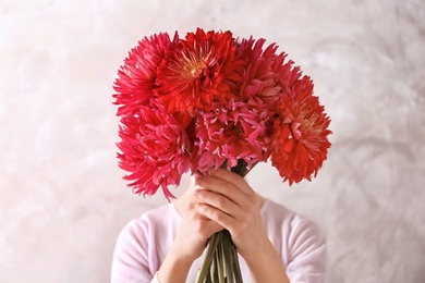 Woman hiding behind beautiful dahlia flowers on color background