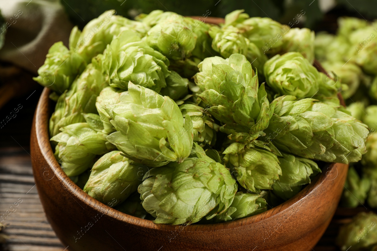 Photo of Fresh hop flowers in bowl on wooden table, closeup