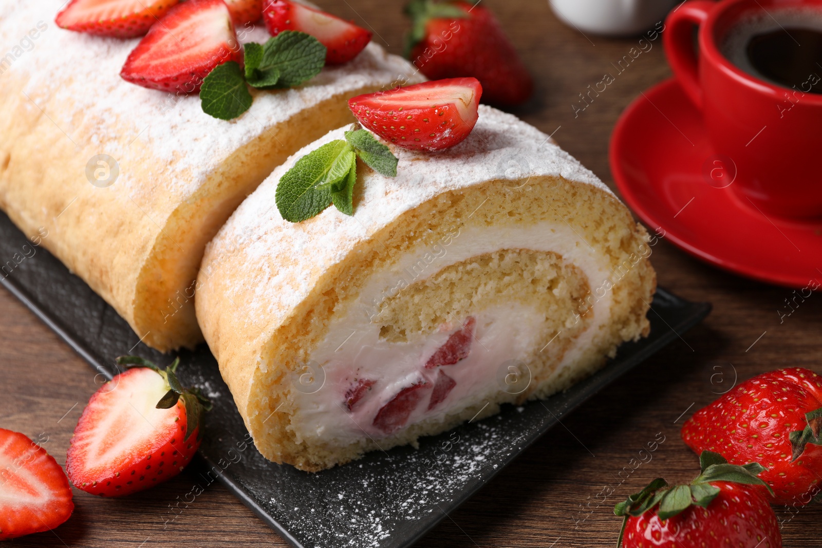 Photo of Delicious cake roll with strawberries and cream on black board, closeup