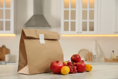 Photo of Paper bag and fresh fruits on white marble table in kitchen