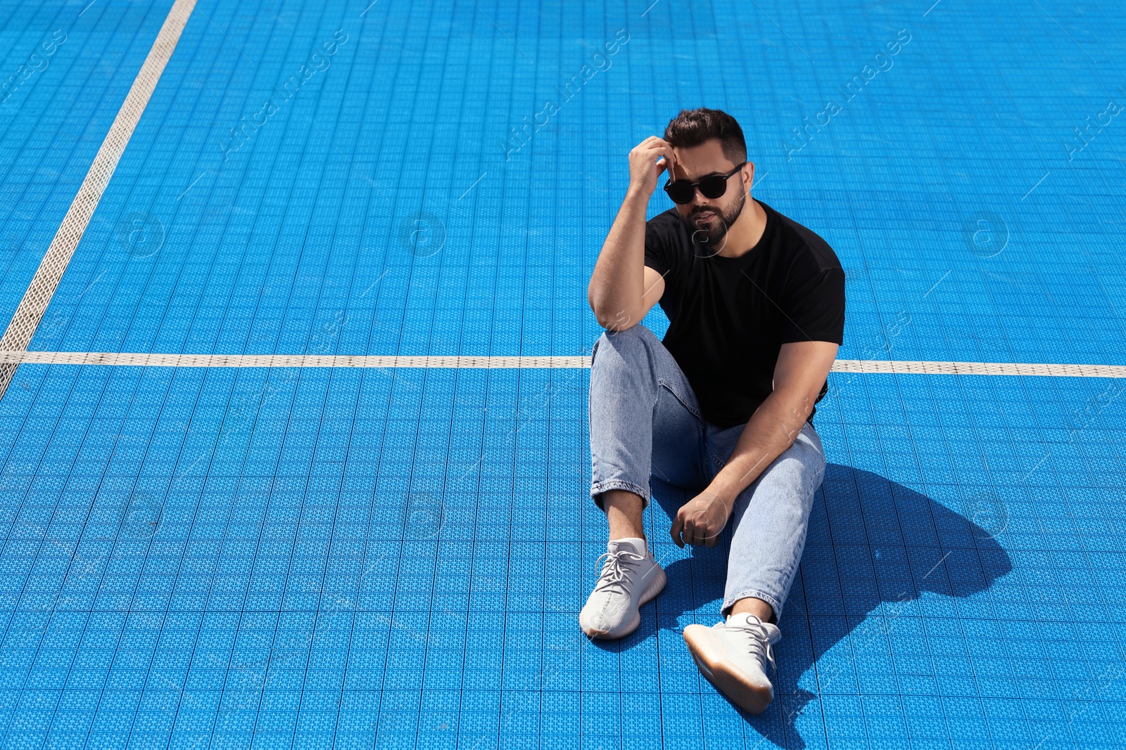 Photo of Handsome man in sunglasses on blue floor covering outdoors, space for text