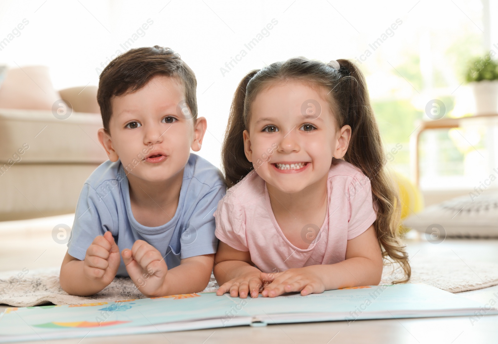 Photo of Cute children reading book on carpet in living room