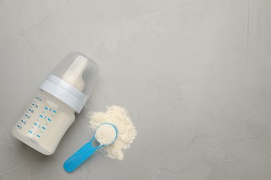 Photo of Feeding bottle with infant formula, scoop of powder and space for text on grey table, flat lay. Baby milk