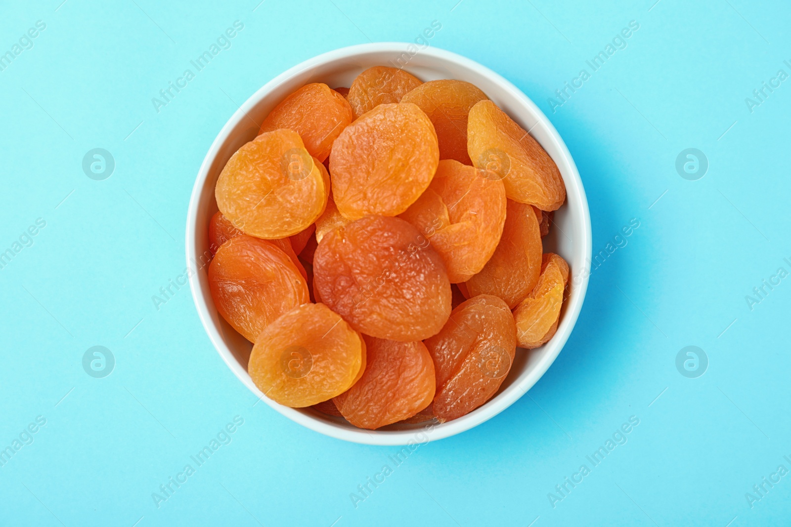 Photo of Bowl with dried apricots on color background, top view. Healthy fruit