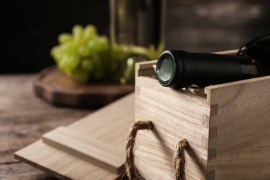 Open wooden crate with bottle of wine on blurred background, space for text