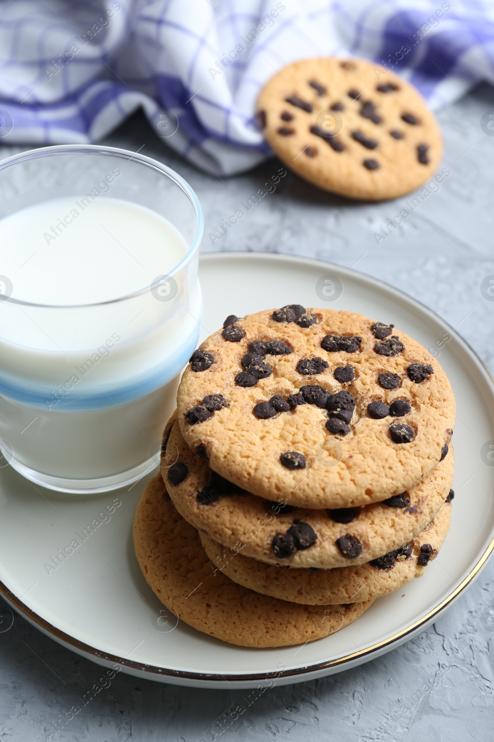 Photo of Delicious chocolate chip cookies and glass of milk on grey textured table