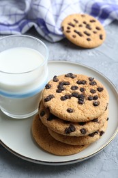 Photo of Delicious chocolate chip cookies and glass of milk on grey textured table