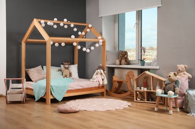 Photo of Stylish child room interior with wooden bed in shape of house and toys