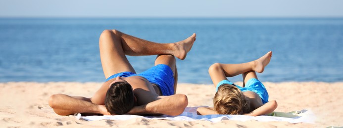 Image of Father and son lying on sandy beach near sea. Banner design