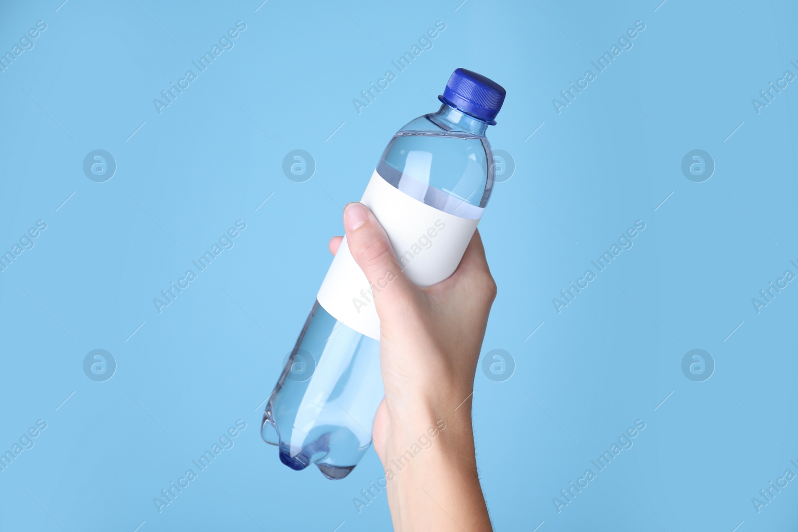 Photo of Woman holding plastic bottle with soda water on light blue background, closeup