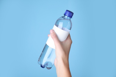Photo of Woman holding plastic bottle with soda water on light blue background, closeup