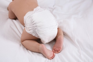 Photo of Cute baby in dry soft diaper on white bed, closeup