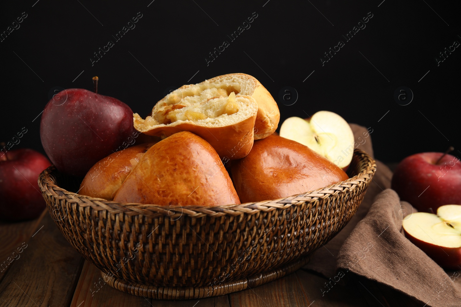 Photo of Delicious baked apple pirozhki in wicker basket and fruits on wooden table