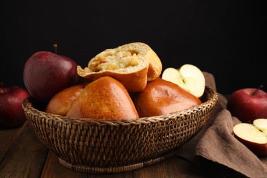 Photo of Delicious baked apple pirozhki in wicker basket and fruits on wooden table