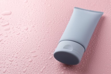 Photo of Moisturizing cream in tube on pink background with water drops, closeup. Space for text