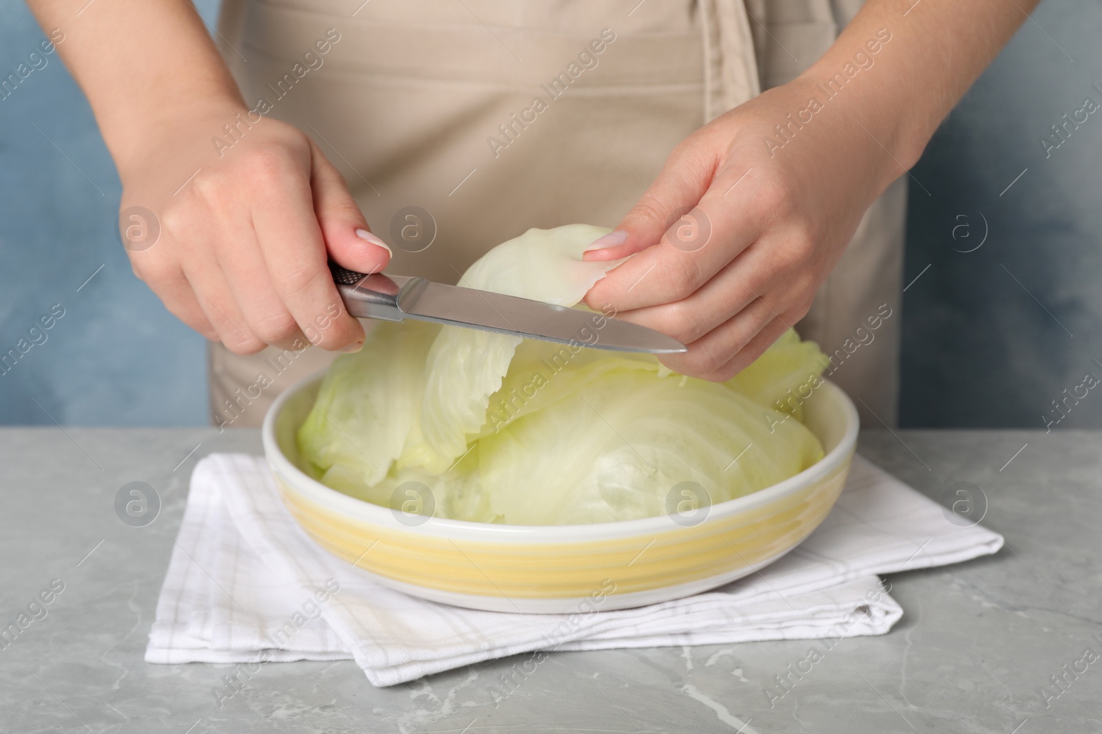 Photo of Woman preparing stuffed cabbage rolls at light grey table, closeup