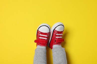 Photo of Little child in stylish red gumshoes on yellow background, top view