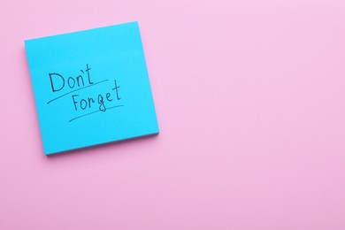 Photo of Paper note with phrase Don't Forget on pink background, top view. Space for text